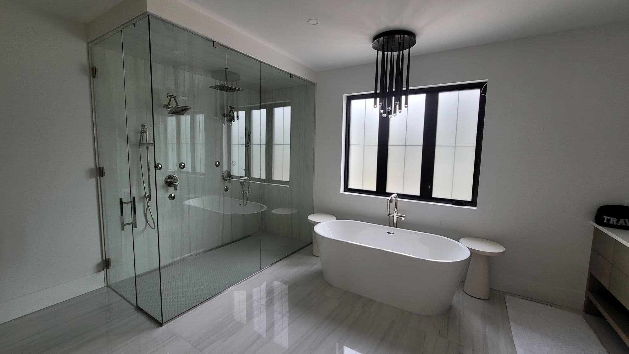 Large custom shower in frameless glass beside a freestanding soaker tub
