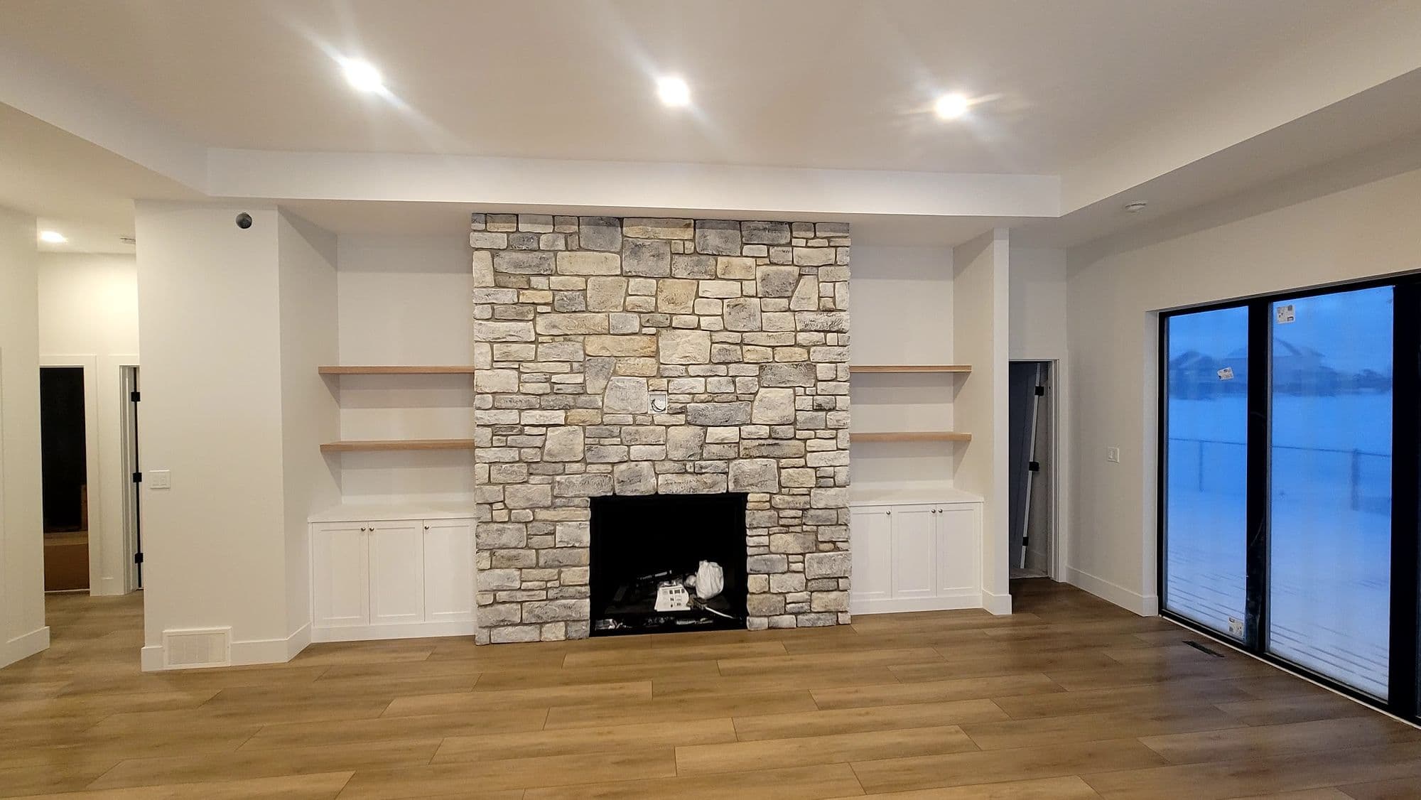 Stone fireplace surround flanked by white built-in cabinets and open shelves
