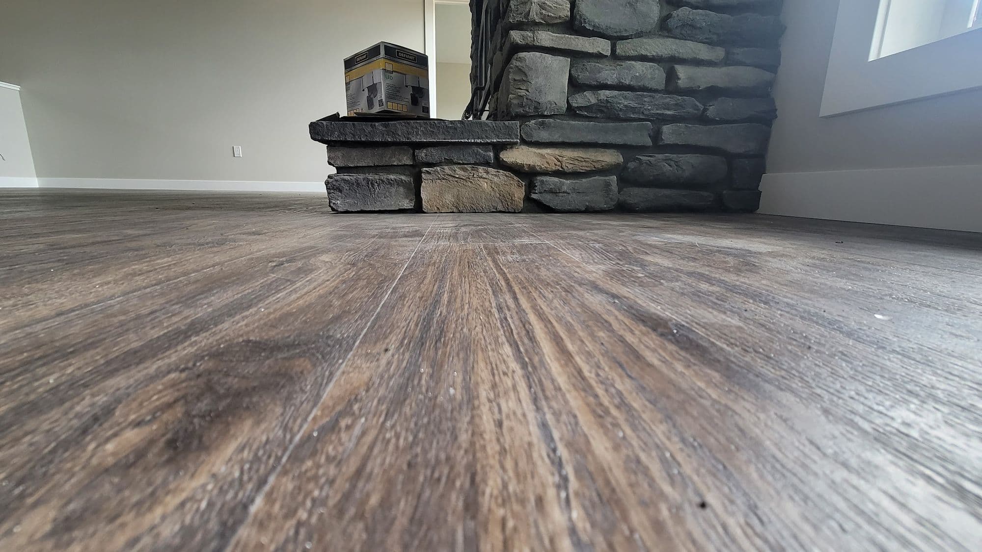 Wide-plank flooring running up to a stone hearth in an empty room